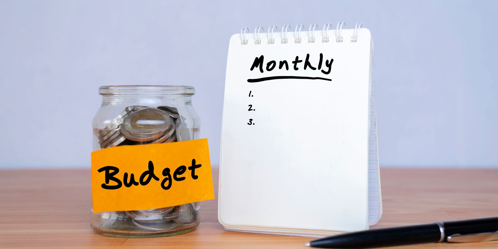 A jar of coins labelled Budget next to a notepad headed Monthly