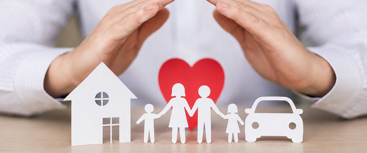 Hands protecting paper cutouts of a house, family and car, representing insurance cover